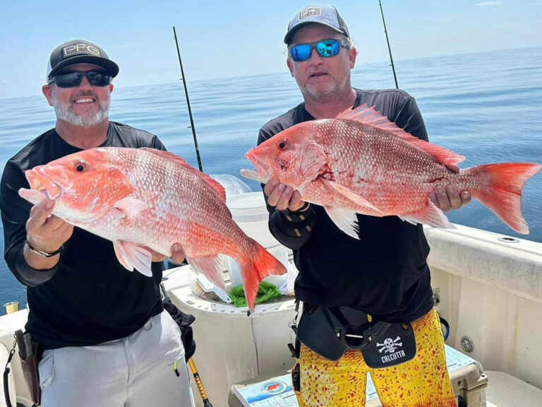 Two men display American red snapper caught from the deck of a charter boat.