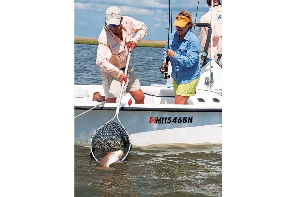 Fisherman netting a giant redfish for a lady angler in the northern Gulf of Mexico